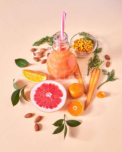 Fresh juicy detox smoothies in glass cup with orange berries, vegetables, fruits, almonds on a yello Stock photo © artjazz