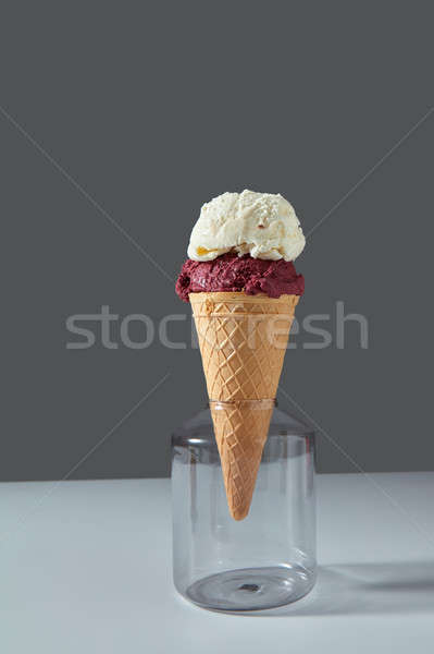 A balls of berry and vanilla ice cream in a waffle cone stands in a glass jar on a gray background o Stock photo © artjazz
