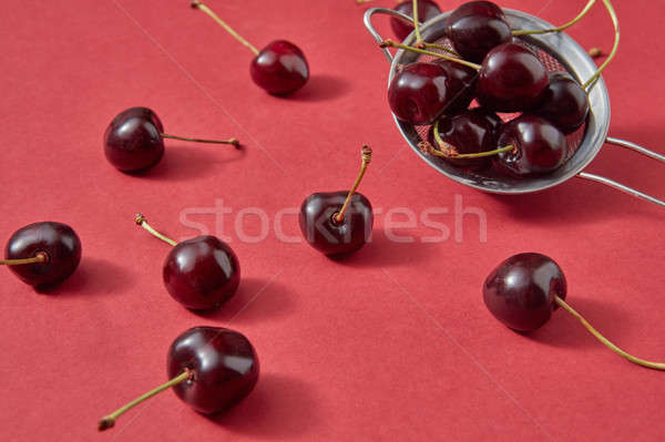 Close-up red ripe sweet cherry berries in a colander and around it on a red paper. Stock photo © artjazz