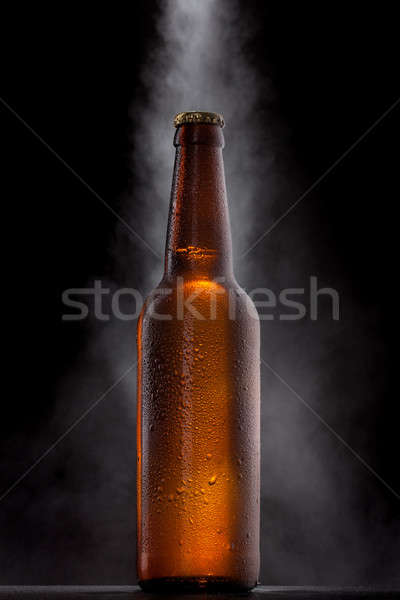 Cold beer bottle with drops, frost and vapour on black Stock photo © artjazz