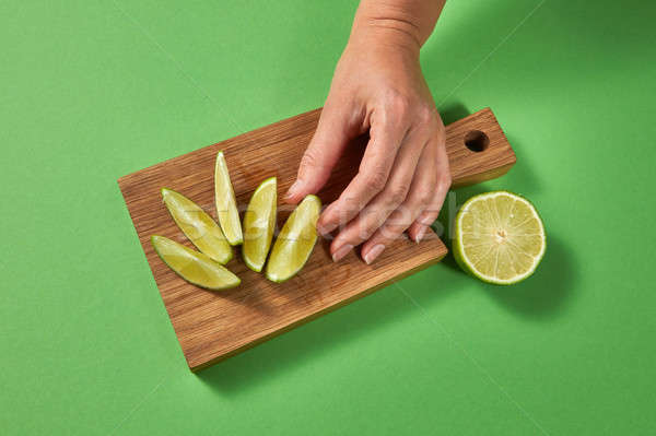 A woman's hand takes a slice of organic fresh green lime on a wooden cutting board. Slices of lime o Stock photo © artjazz