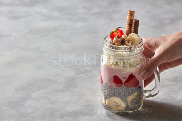 Glass with a layered breakfast from yogurt, strawberry, chia pudding with a banana in the female han Stock photo © artjazz