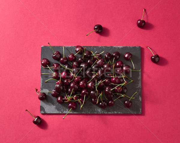 Delicious sweet cherry on a black stone board on red paper background with place for text. Flat lay. Stock photo © artjazz