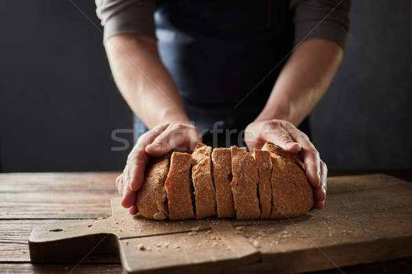 Fresh home slice bread in male's hands on the wooden board. Stock photo © artjazz