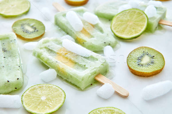 Homemade kiwi ice cream on a stick with pieces of ice, lime and kiwi on a gray background. Food patt Stock photo © artjazz