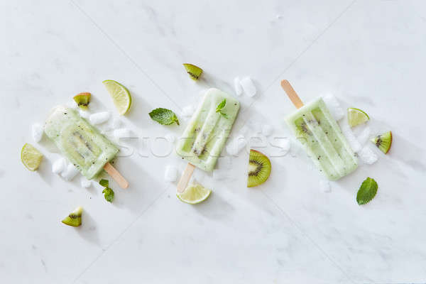 Sticks of ice cream with kiwi and lime on a gray marble background with pieces of ice and mint leave Stock photo © artjazz