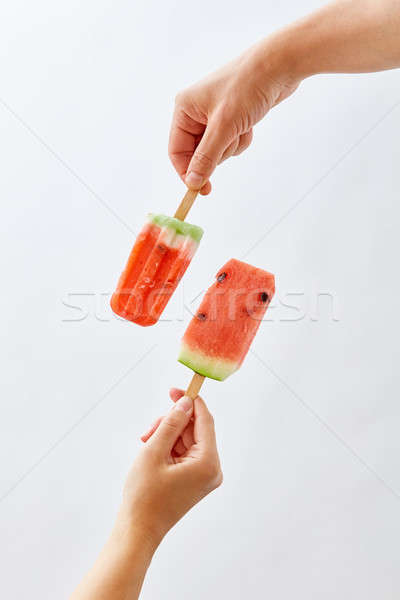 A man's hand holds a slice of watermelon on a stick, in the form of an ice cream, and a red ice crea Stock photo © artjazz