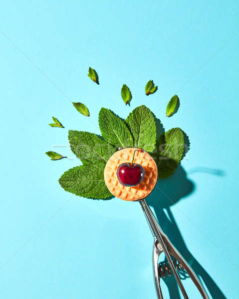 Flat lay of spoon for ice cream with mint leaves, biscuit and cherry on a blue background with hard  Stock photo © artjazz