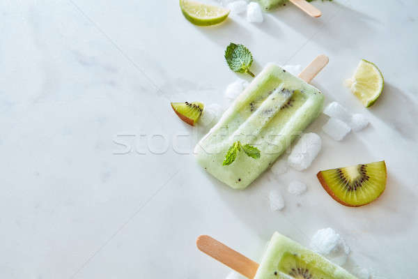 Stock photo: Lime minty frozen smoothies on a stick with pieces of kiwi presented on a gray marble background wit