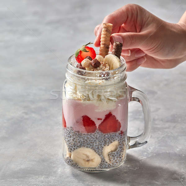 Layered berry and chia seeds smoothies in a glass jar, girls hand decorate cookies on a gray concret Stock photo © artjazz