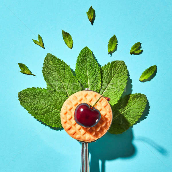 Flat lay of spoon for ice cream with mint leaves, biscuit and cherry on a blue background with hard  Stock photo © artjazz