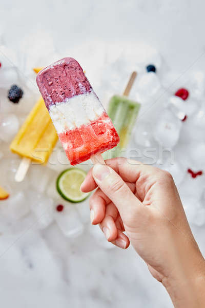 Homemade frozen smoothies on a stick, holding a female hand against a background of ice cubes with v Stock photo © artjazz