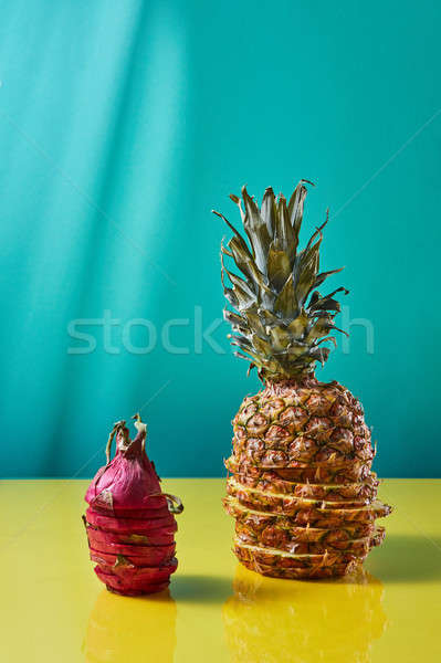 Stock photo: Sliced pineapple and sliced pitaya on a blue-yellow paper background. Exotic fruits