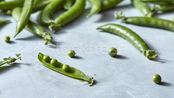 Organic green pods of young green peas opened on a gray marble table. Stock photo © artjazz