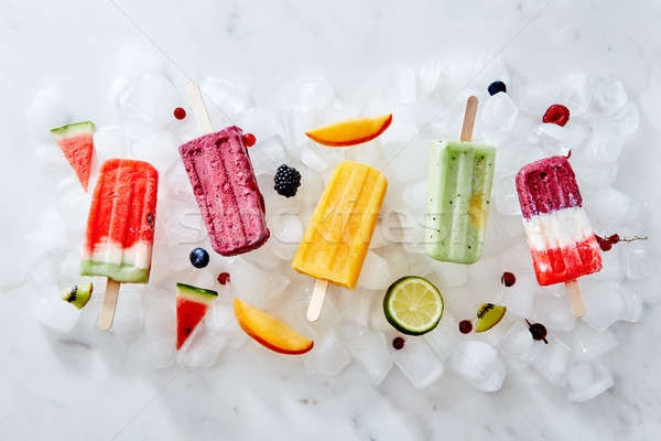 Different ice cream on a stick and different pieces of fruit and berries on ice cubes. Flat lay Stock photo © artjazz