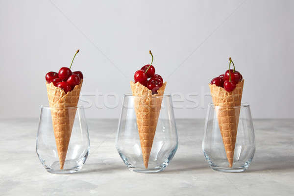 Three waffle cones with fresh ripe cherries in glasses on a gray Stock photo © artjazz