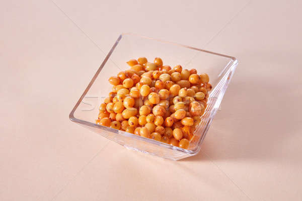 Yellow ripe sweet berries - sea buckthorn in the glass bowl on a beige paper background. Stock photo © artjazz