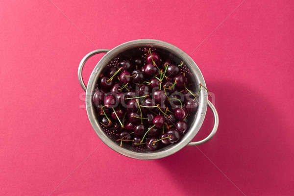 Summer ripe sweet cherry berries in a colander on a red paper background. Top view. Stock photo © artjazz