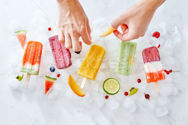 The woman's hands decorate the ice cream on a stick with bits of juicy fruit. Summer dessert. Flat l Stock photo © artjazz