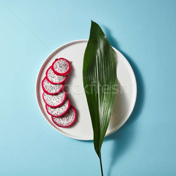 Dragon fruit or pitaya slice in plate with green leaves on blue background Stock photo © artjazz