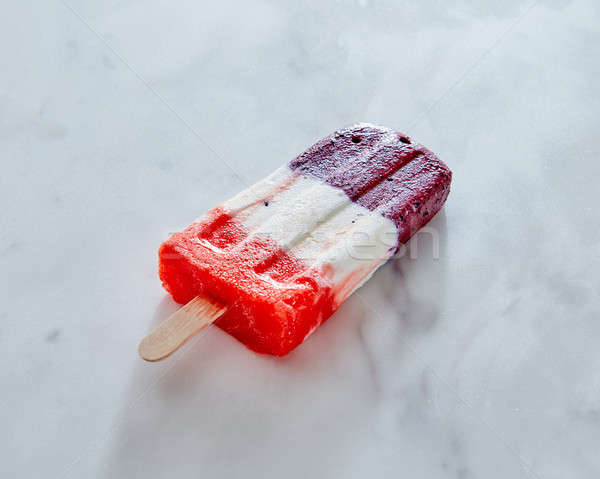 A multicolored creamy berry ice cream on a stick is represented on a gray marble background with a c Stock photo © artjazz