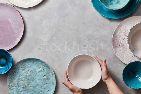 Female hands hold a white ceramic bowl on a gray marble table. Clay handcraft bowls, plates of diffe Stock photo © artjazz