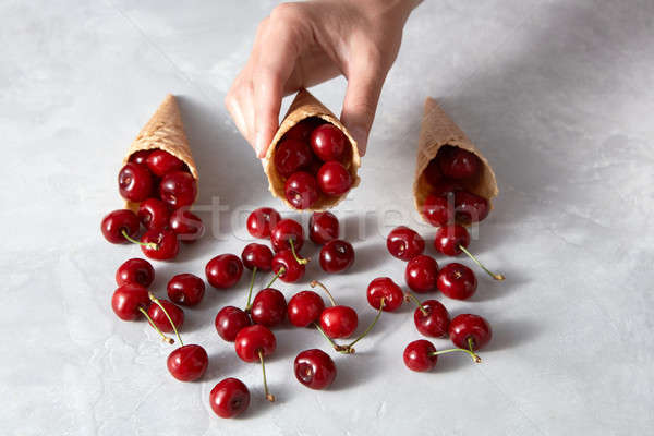 The woman's hand takes crispy wafer cups with ripe red cherries on a gray stone background. Stock photo © artjazz
