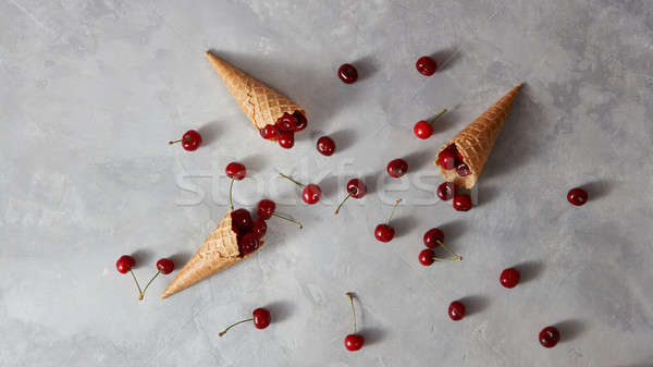 Pattern of freshly picked ripe cherries in a sweet wafer cones on a gray concrete table. Cherry on a Stock photo © artjazz