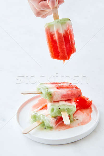 Ice cream lolly in a plate with splashes. A woman's hand holds a melting ice cream on a white marble Stock photo © artjazz