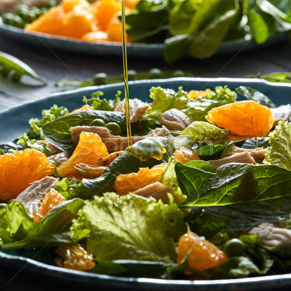 Stock photo: A stream of olive oil pours into the prepared salad with natural green vegetables, chicken pieces, o