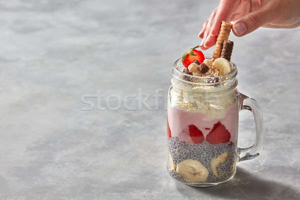 Healthy breakfast in the hand: yogurt parfait with chia pudding, strawberries and banana in glass on Stock photo © artjazz