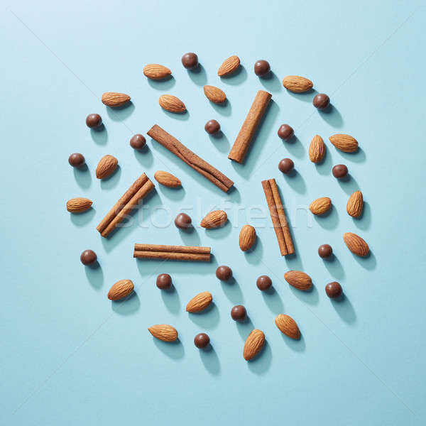 A circle of cinnamon sticks, almonds and chocolate balls on a blue paper background. Flat lay Stock photo © artjazz