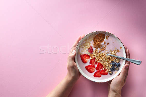 Woman's hands holding a bowl of organic yogurt smoothie with strawberries, banana, blueberry, oat fl Stock photo © artjazz