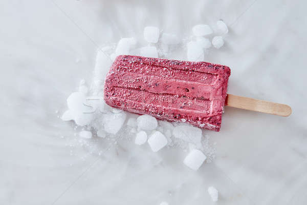 Bitten fresh red berry frozen popsicle with ice on a light marble background, top view. Room for you Stock photo © artjazz
