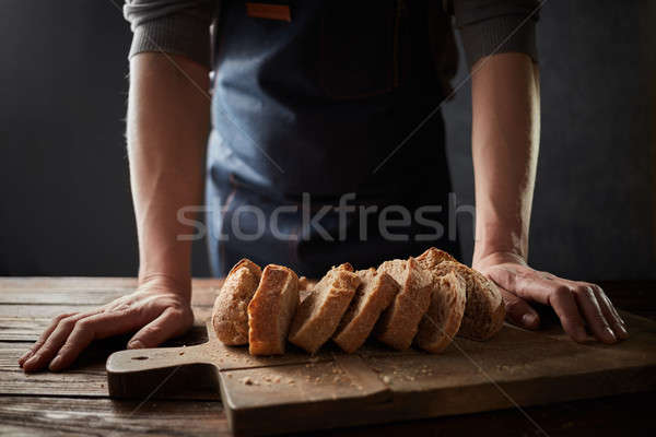 Baker man holding rustic organic loaf of bread in hands rural bakery. Stock photo © artjazz