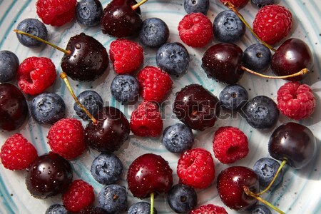 Close-up of summer organic berries - cherry, raspberry, blueberries in water droplets in the blue pl Stock photo © artjazz