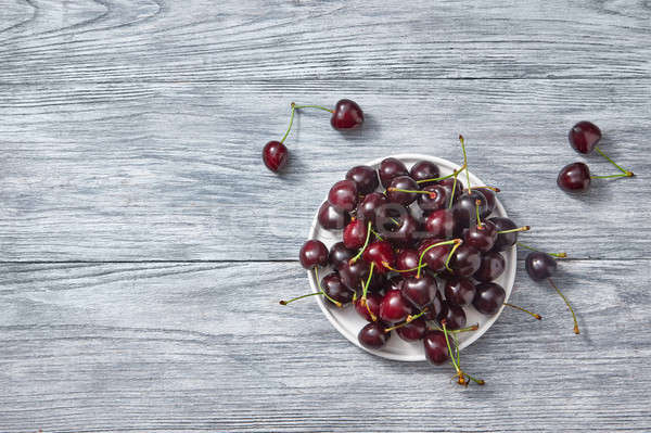 Ripe sweet cherry on a white plate on a gray wooden background. Place for text. Stock photo © artjazz