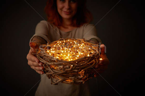 Smiling girl holding a wreath of twigs with yellow lights around a black background. Stock photo © artjazz