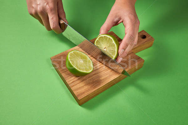 A woman cut a natural green lime into two pieces on a wooden bro Stock photo © artjazz