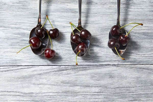 Summer cherry colorful pattern with spoons of berries on gray wooden background. Stock photo © artjazz