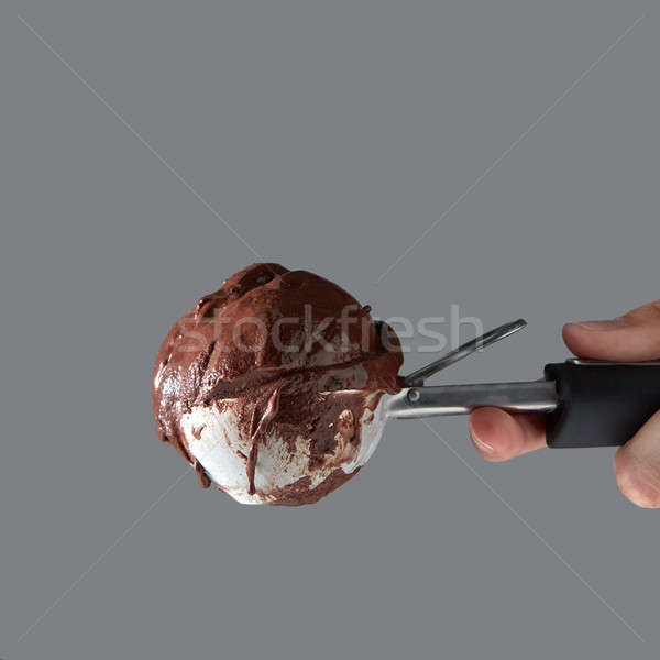 A ball of chocolate homemade dessert in a metal spoon for ice cream holds a woman's hand on a gray b Stock photo © artjazz