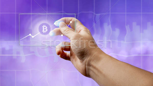 Stock photo: A man holds a glass screen with a bitcoin symbol and a crypto currency graph