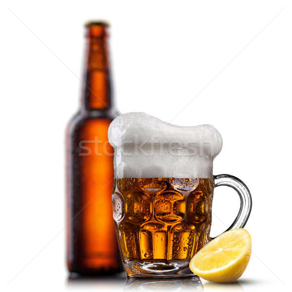 Beer in glass with water drops and lemon against bottle isolated Stock photo © artjazz