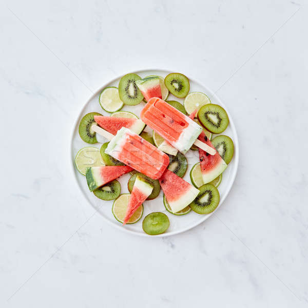 Multicolored berry frozen smoothies lolly with pieces of kiwi, lime, watermelon and ice cubes in a p Stock photo © artjazz