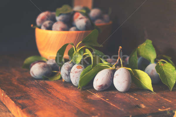 Stock photo: Fresh plums with green leaves in wooden pot on the dark wooden t