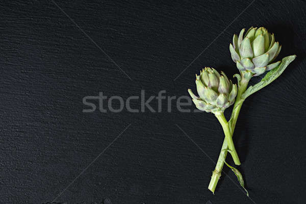 Two cones fresh green artichoke on a black stone surface.  Top v Stock photo © artsvitlyna