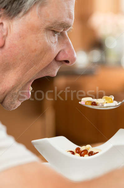 Senior man eating a spoon of vitamins Stock photo © backyardproductions