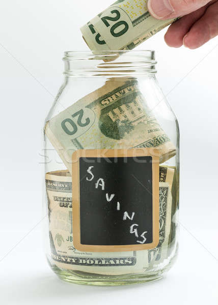 Hand inserting money into saving jar or bank Stock photo © backyardproductions