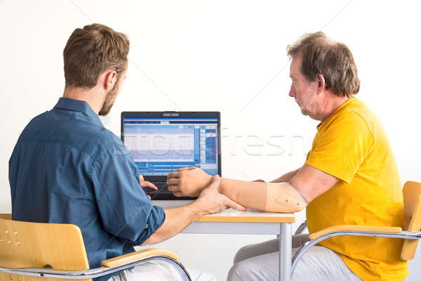 Medical professional and amputee work together. Computer-based arm-prosthesis adjustment. Stock photo © belahoche