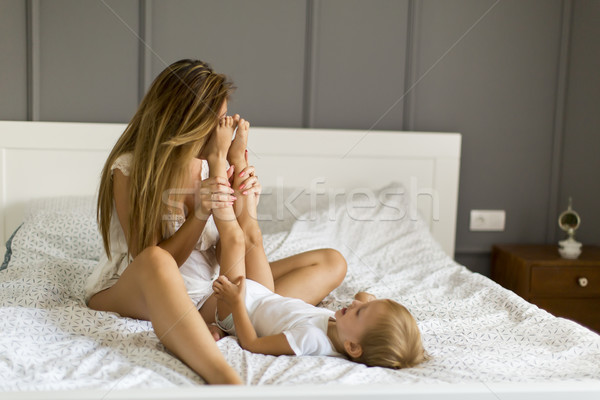 Stock photo: Young happy mother playing in a white bed enjoying a sunny morni